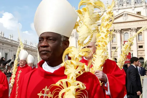 Reuters A mid-crop of Cardinal Peter Turkson looking solemnly ahead while wearing traditional religious robes along with others outside St. Peter